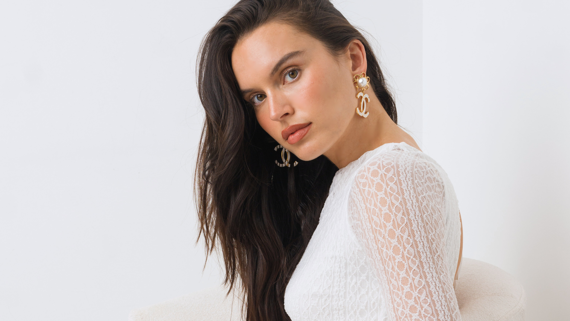 Woman wearing Chanel earrings in a white lace dress and white background